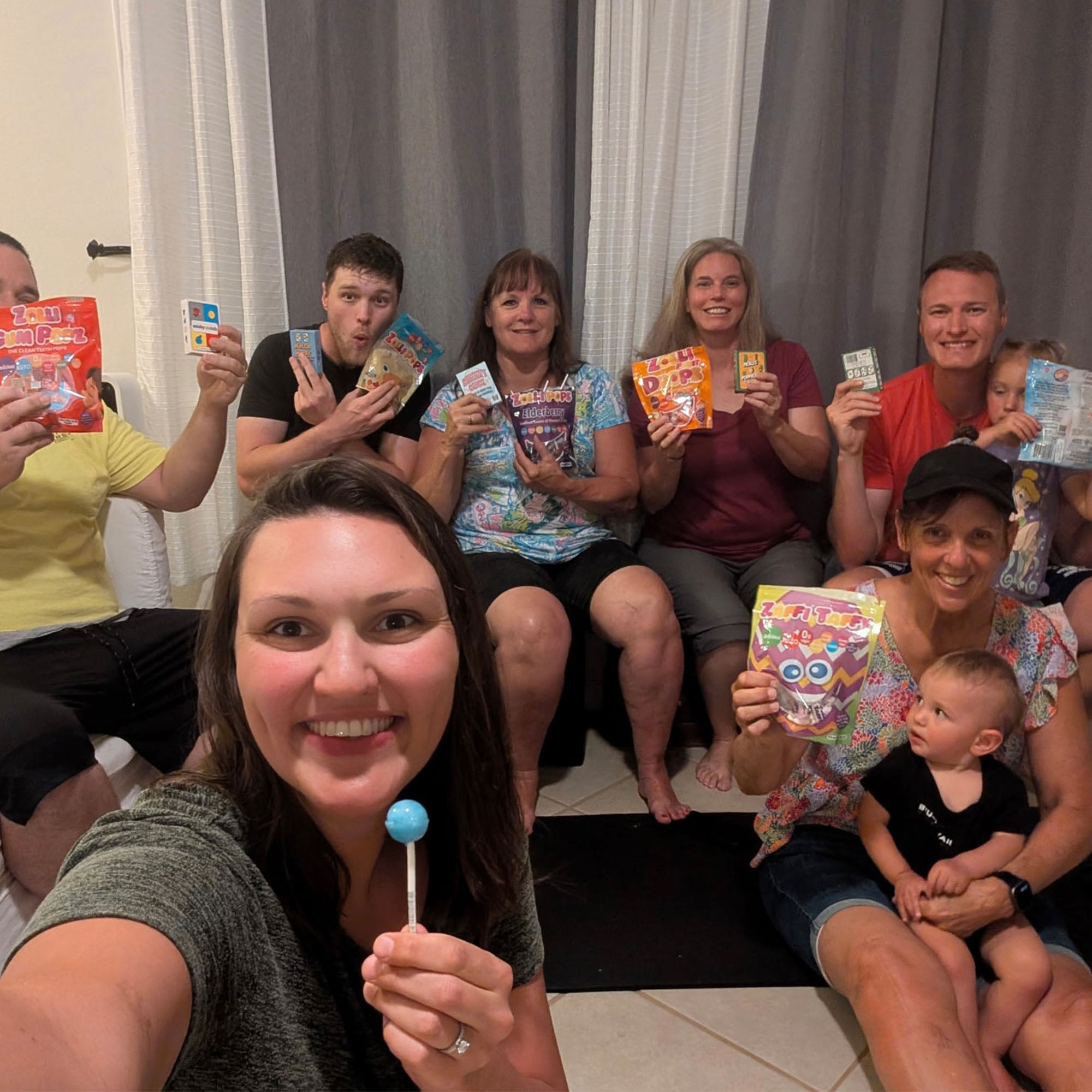 Group of people sitting together, holding colorful packages and a lollipop.