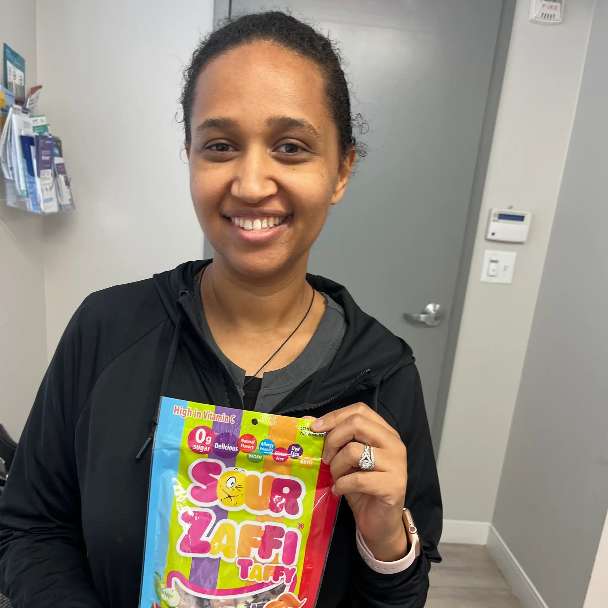 Woman holding a colorful package of Sour Zaffi Taffy in an indoor setting.