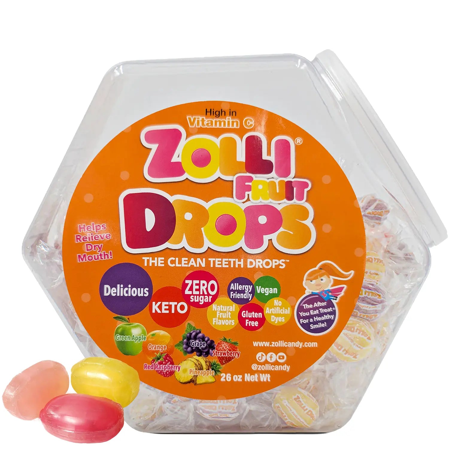 A clear hexagonal plastic container of Zolli Fruit Drops candy with a large orange label, shown on a white background with three loose fruit drops in front.
