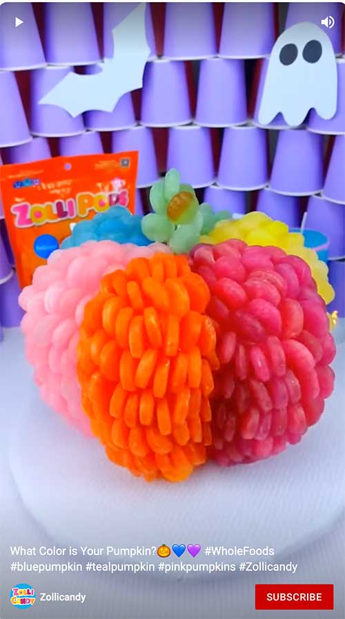 Colorful pumpkin made of candy displayed against a purple background with ghost and bat decorations.